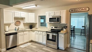 A kitchen with white cabinets, a microwave, stove, dishwasher, and a welcome sign.