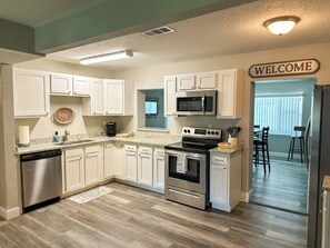 A kitchen with white cabinets, a microwave, stove, dishwasher, and a welcome sign.