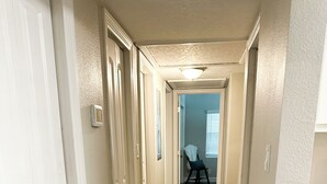 A hallway with wooden flooring, white walls, and a door on the left.