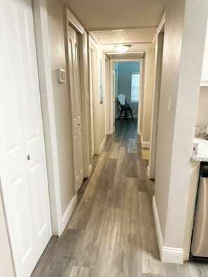 A hallway with wooden flooring, white walls, and a door on the left.