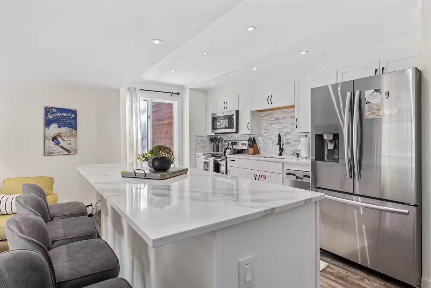 A modern kitchen with a large island, stainless steel appliances, and a dining area with grey sofas.