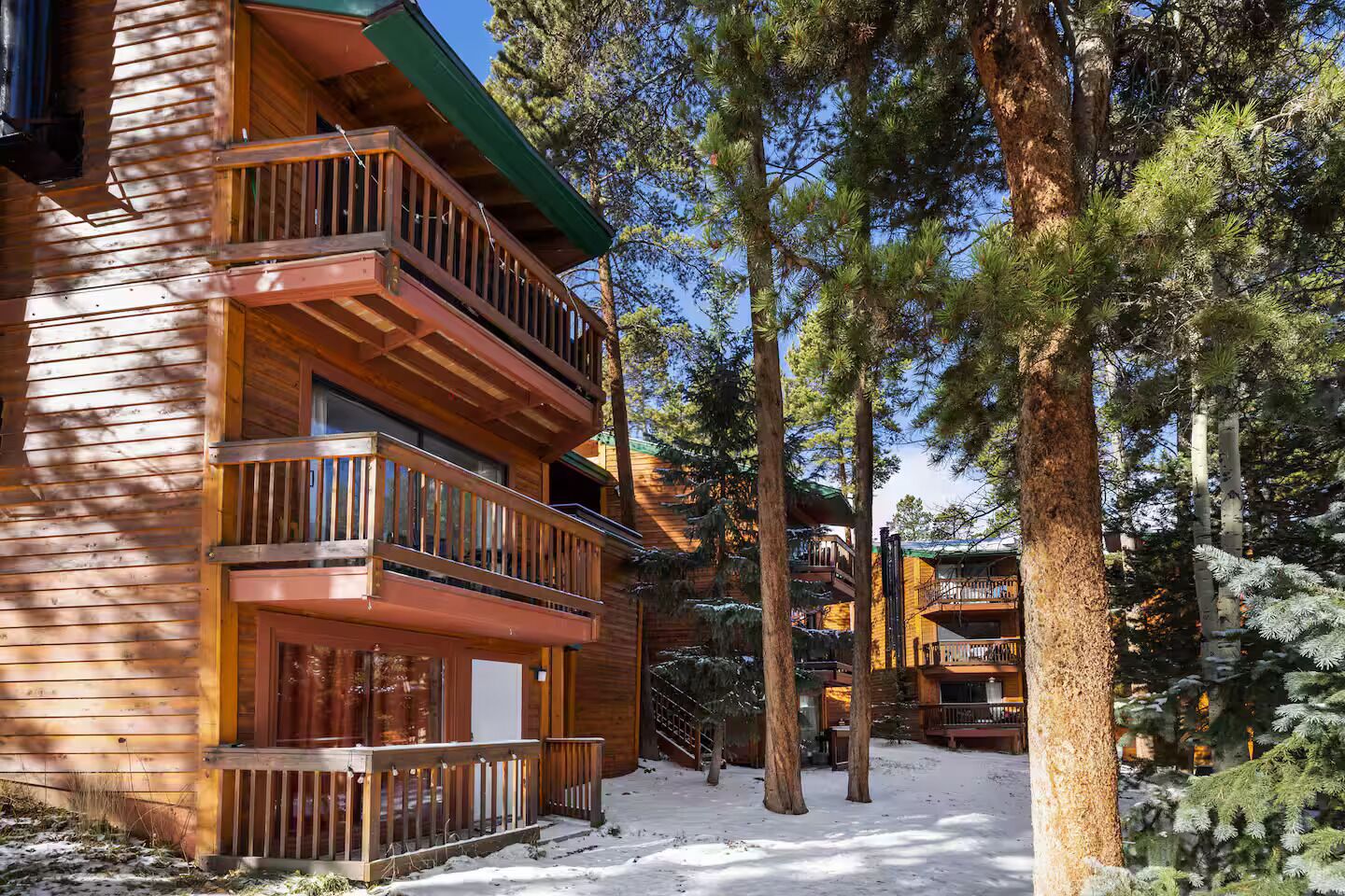 A multi-story log cabin with balconies, surrounded by tall pine trees.