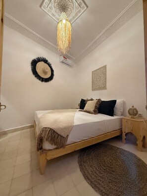 Ein Schlafzimmer mit einem hölzernen Bett, einem gemusterten Teppich, einer dekorativen Deckenleuchte und Wandbildern.