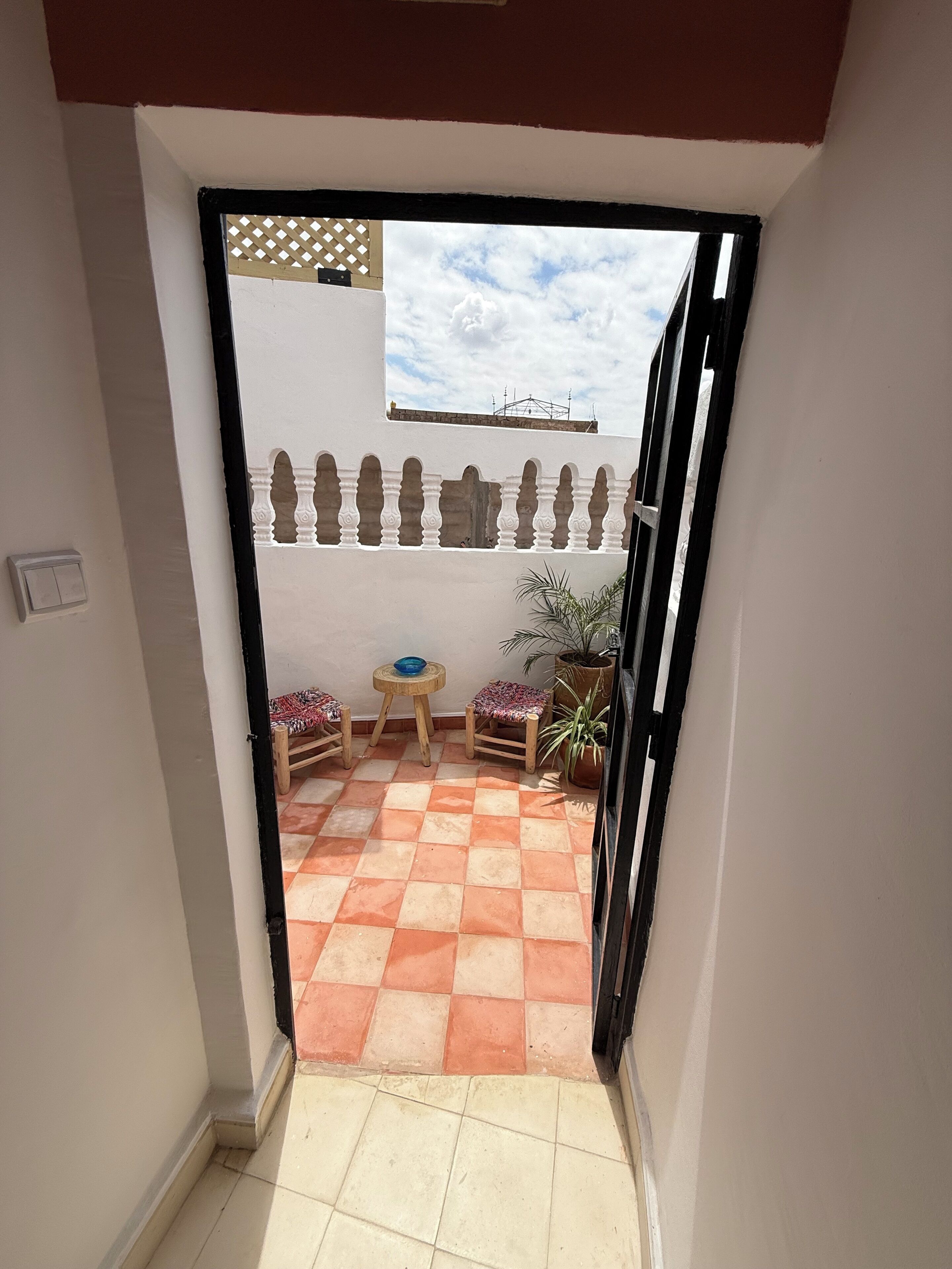 A corridor leading to a patio with a checkered floor, a small round table, two chairs, and a potted plant.
