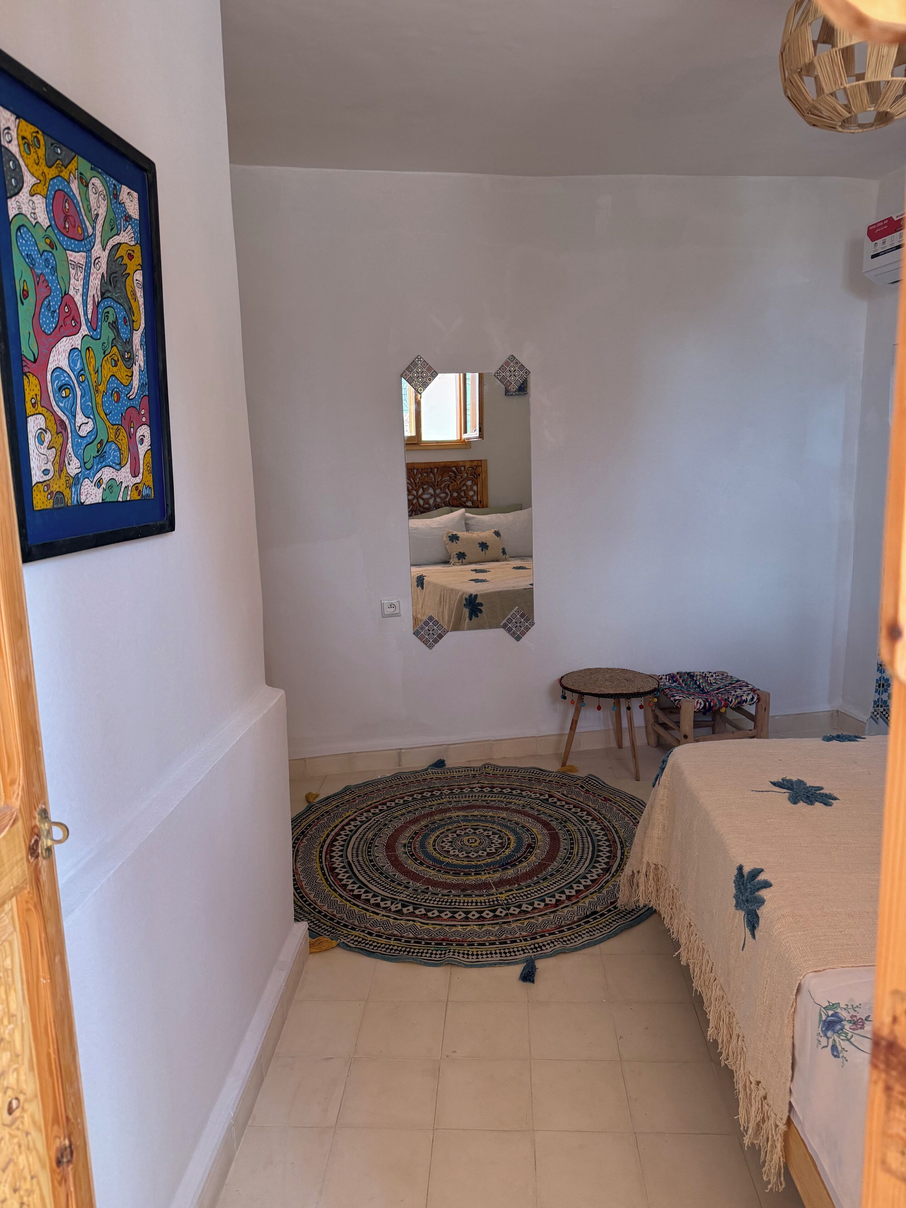 Een slaapkamer met een bed, een spiegel, een klein tafeltje, een stoel en een kamerkleed met een patroon.