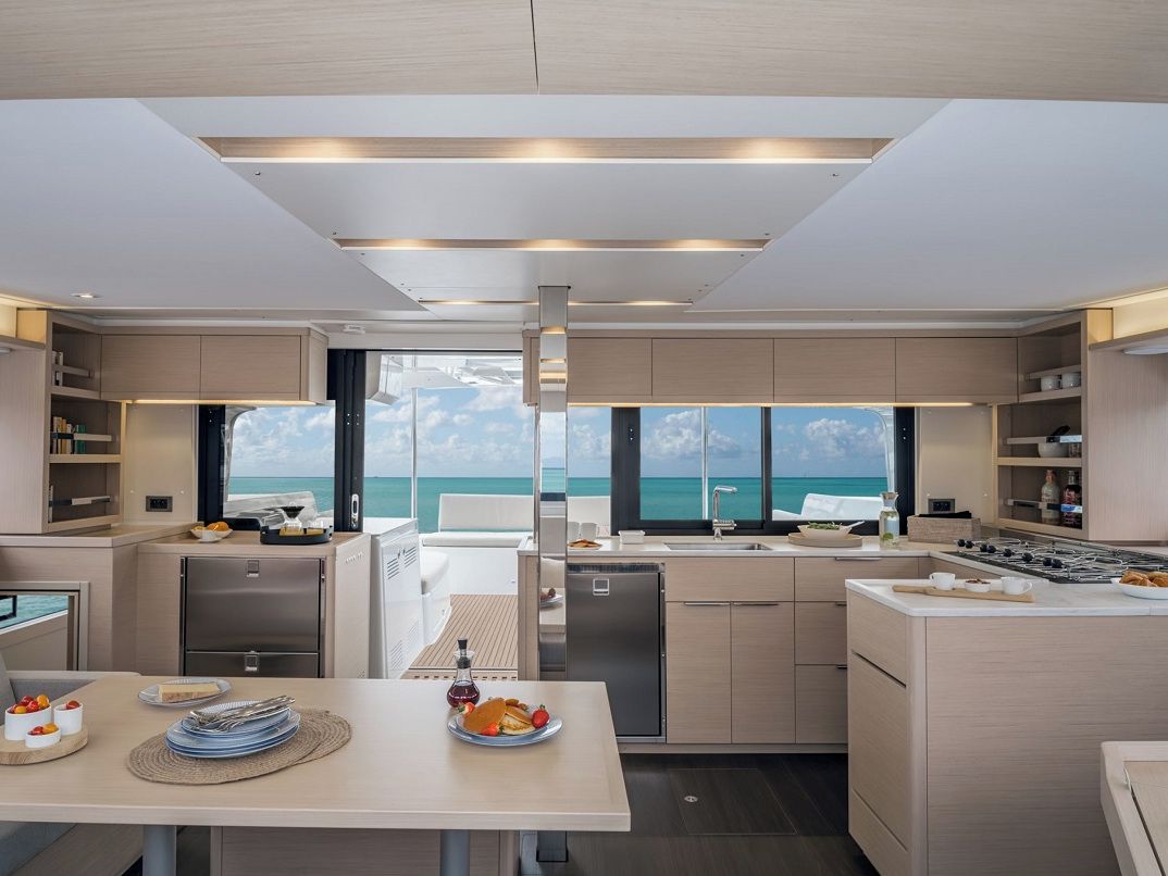 Une cuisine moderne avec vue sur la mer, comprenant un coin repas avec une table dressée pour deux personnes, un réfrigérateur et une cuisinière.