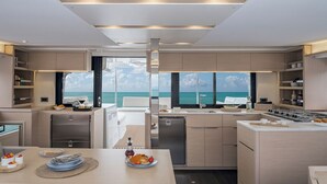 A modern kitchen with a view of the sea, featuring a dining area with a table set for two, a refrigerator, and a stove. - Sun-kissed Sailing Adventure in Split-Dalmatia, Croatia (Trogir)