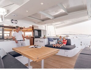 A modern yacht interior with a dining area, a kitchen, and a seating area with a view of the water.