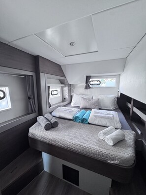 A compact, modern RV bedroom with a bed, pillows, and neatly folded towels.