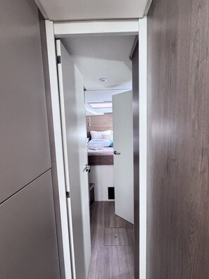 A narrow hallway leading to a bedroom with a bed, a small window, and a door.