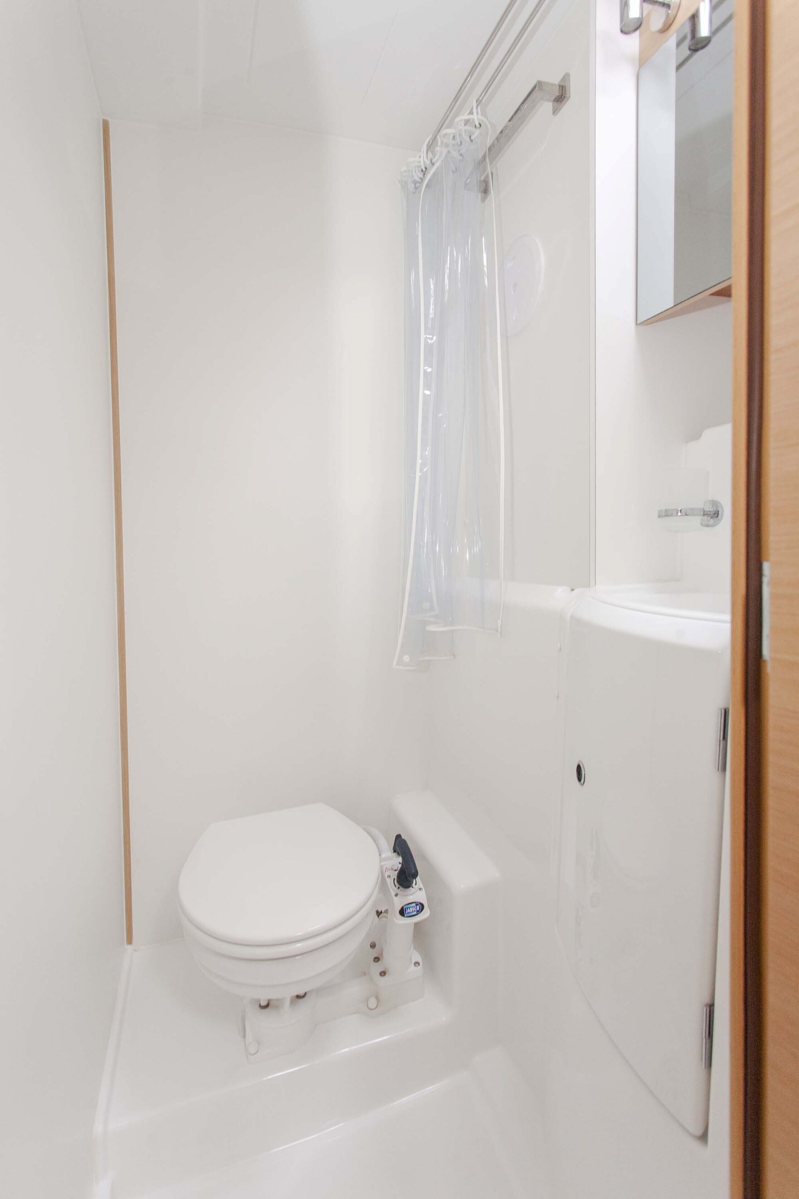 Ein kleines, weißes Badezimmer mit Toilette, Duschvorhang und Spiegel über dem Waschbecken.