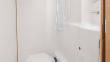 Ein kleines, weißes Badezimmer mit Toilette, Duschvorhang und Spiegel über dem Waschbecken.