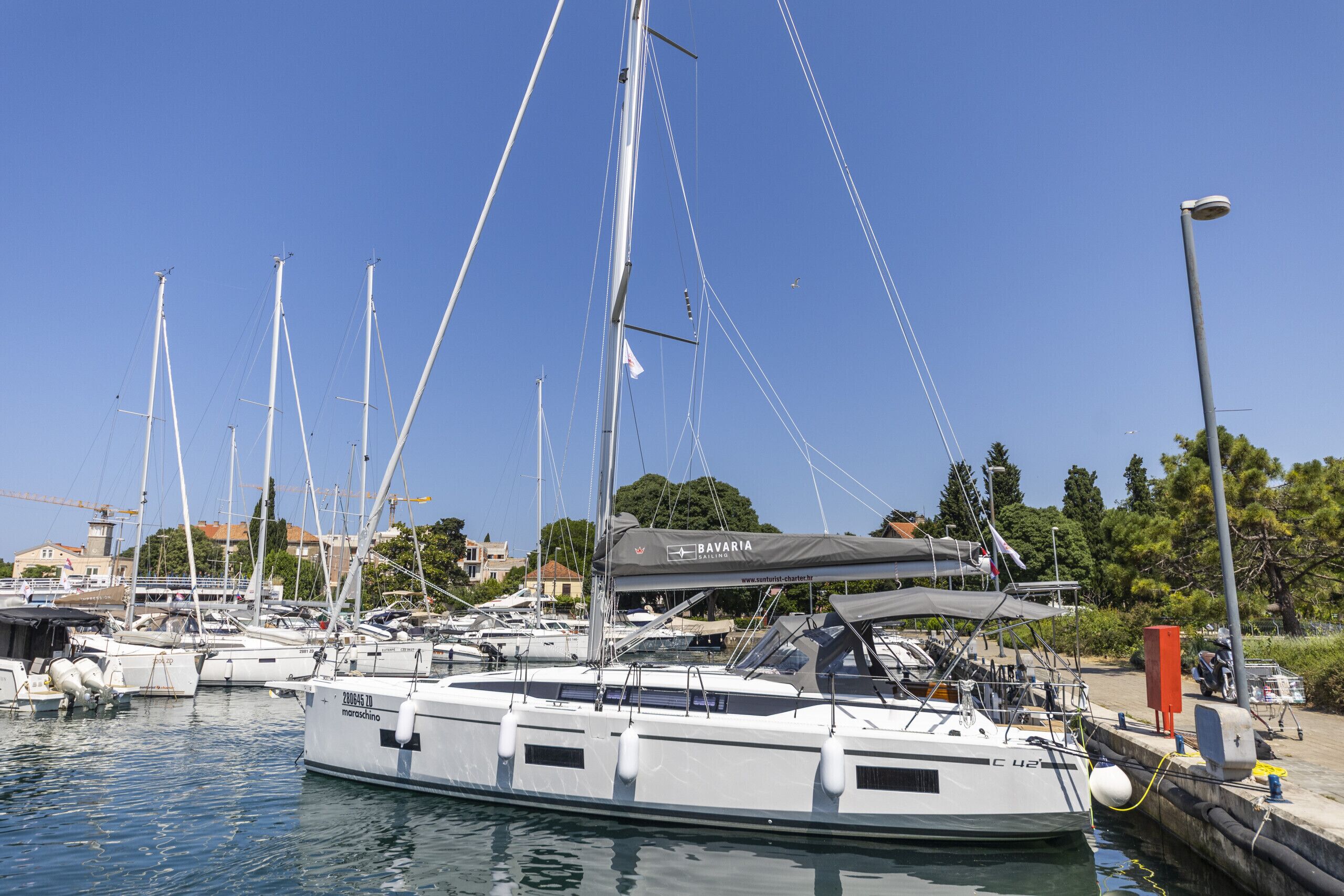 Un port de plaisance où sont amarrés plusieurs voiliers, avec une zone abritée et un bâtiment en arrière-plan.