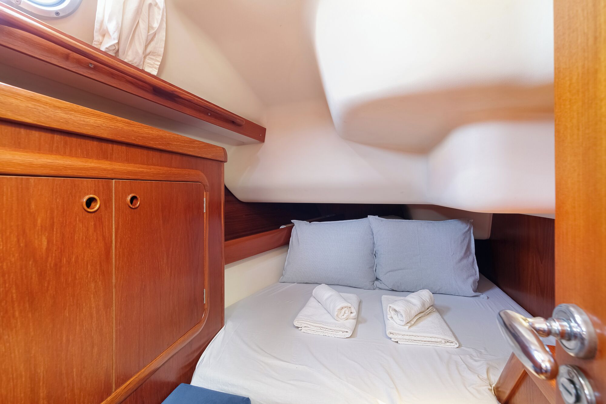 Una cabaña pequeña con cama, dos almohadas, un armario de madera con dos cajones y un ventanal.