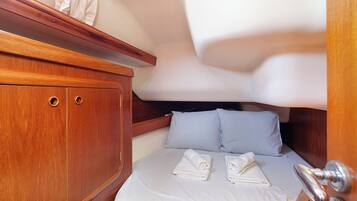 Una cabaña pequeña con cama, dos almohadas, un armario de madera con dos cajones y un ventanal.