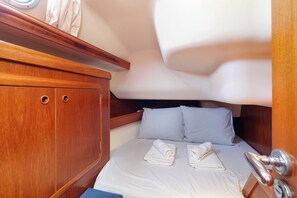Una cabana senzilla amb un llit, dos coixins, un armari de fusta amb dos calaixos i una finestra petita.