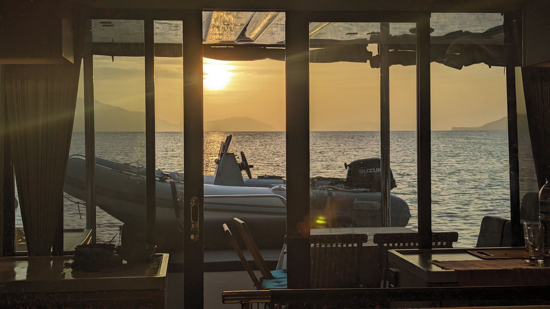 A room with a view of the sea and mountains, a boat, and a table with items on it.