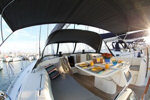 Un pont de bateau équipé d’une table à manger, de sièges et offrant une vue sur le port de plaisance.