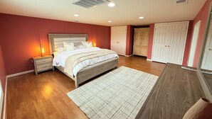 Un dormitorio con cama, mesitas de noche, cómoda, armario y rejilla de ventilación en el techo.