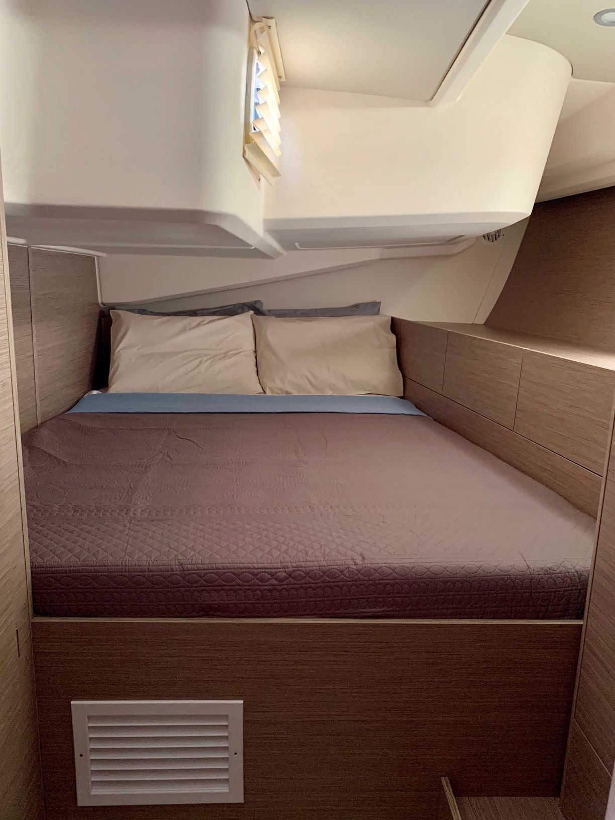 Ein kompakter, gut beleuchteter Raum mit einem Bett, einem kleinen Fenster und einer Belüftungsanlage.