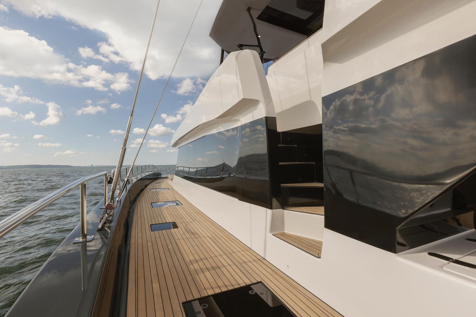 A yacht deck with a wooden floor, white railings, and a large window offering a view of the sea.