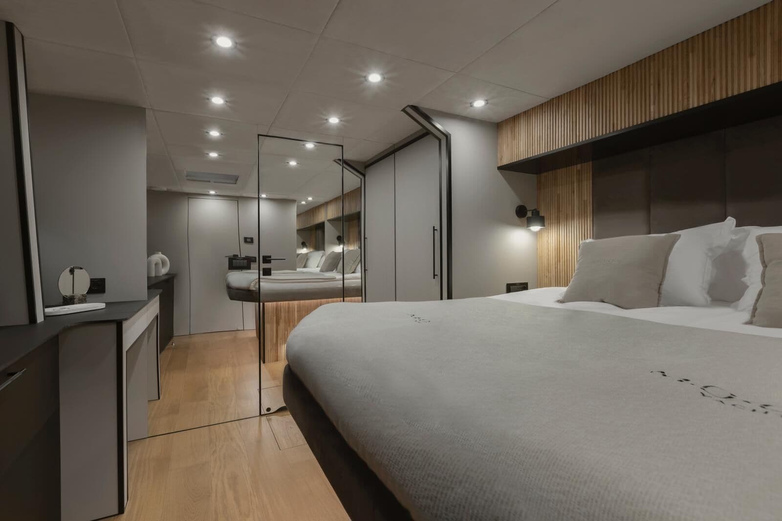 A modern bedroom with a large bed, a wooden headboard, a mirror, and a bedside table.