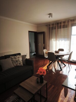 A living room with a sofa, a coffee table, and a dining area with chairs and a table. - Excellent apartment in Matosinhos Sul. Very close to the beach and the subway. (Matosinhos)