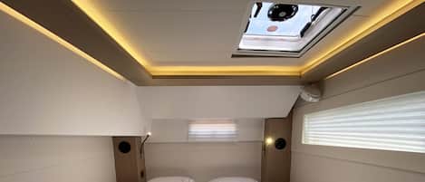 Une chambre d’hôtel de taille réduite, comprenant un lit, deux oreillers, une table de chevet, une fenêtre avec stores et un puits de lumière.