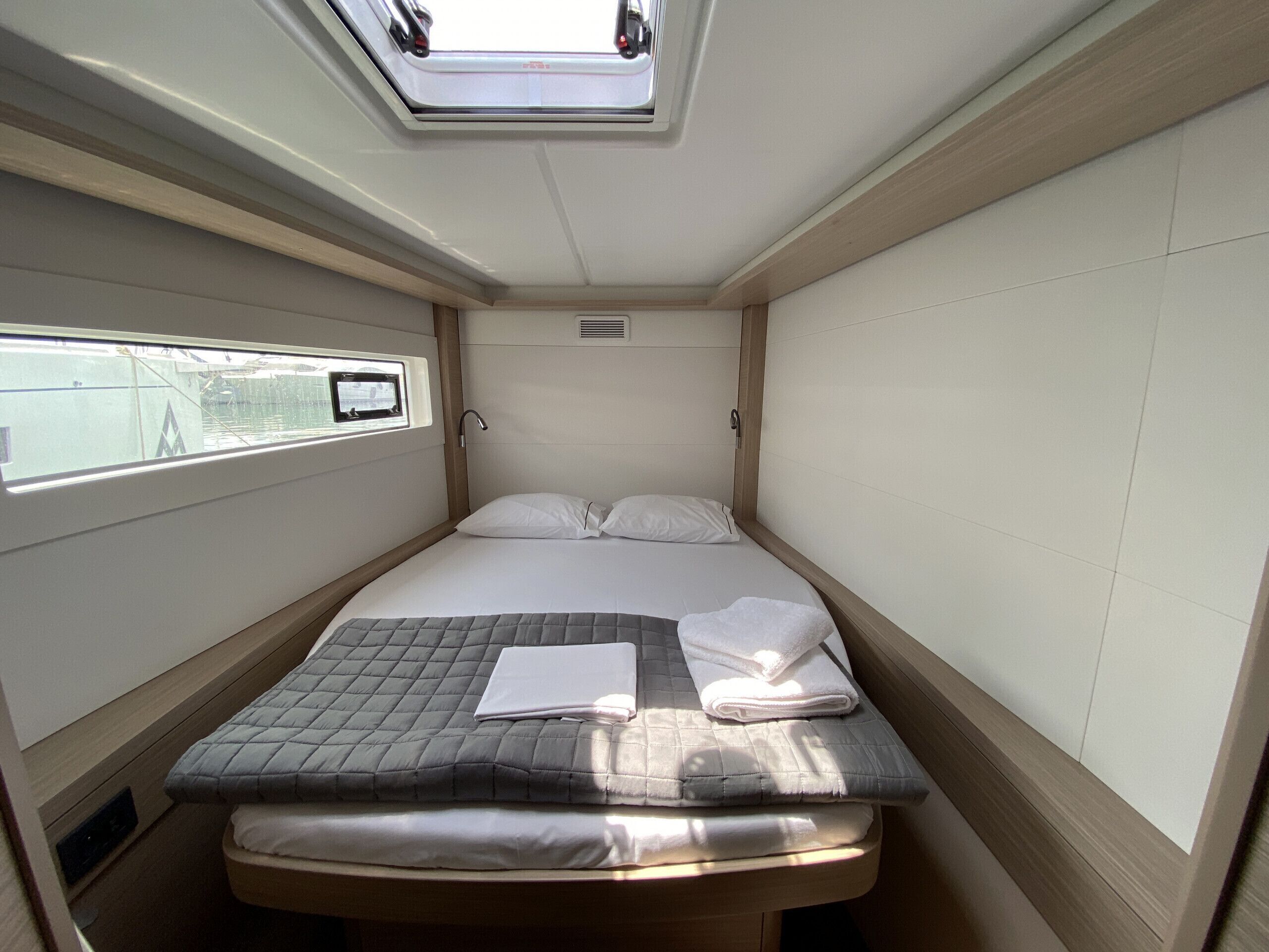 A compact bed with a quilted mattress, a small window with a view, and a skylight above.