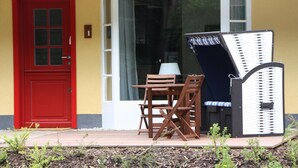 A red door, a white-framed window, and a wooden table with chairs outside a building. - Apartment mit Strandkorb in Uckeritz (Ueckeritz)