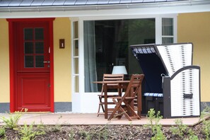 A red door, a white-framed window, and a wooden table with chairs outside a building. - Apartment mit Strandkorb in Uckeritz (Ueckeritz)
