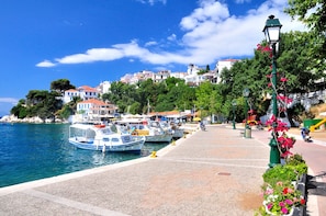 A coastal town with boats docked, a paved walkway, and buildings with red roofs.