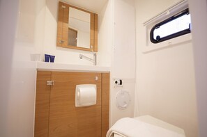 A bathroom with a wooden vanity, a mirror, a towel dispenser, and a window. - Sun-Kissed Sailing Adventure in the Ionian Islands, Lefkada (Lefkada)