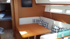A compact RV interior with a wooden table, cushioned seating, a mounted TV, and a window for natural light.