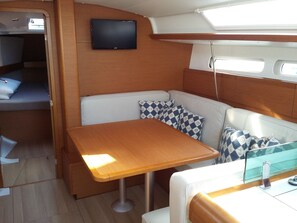 A compact RV interior with a wooden table, cushioned seating, a mounted TV, and a window for natural light.