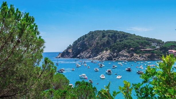 A coastal scene with boats on the water, a rocky island, and buildings on the shore.