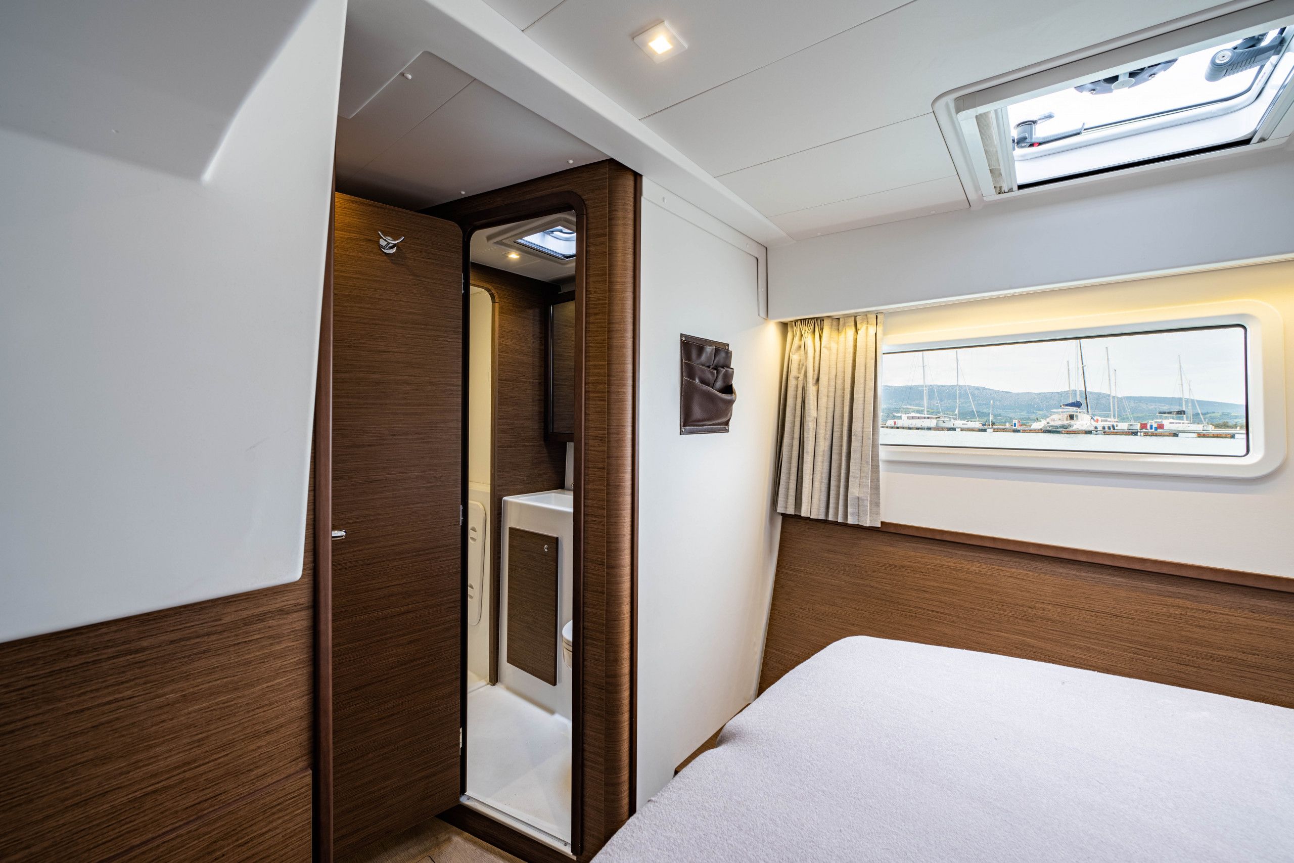 A compact room with a bed, a small bathroom, and a window with a view of boats and hills.