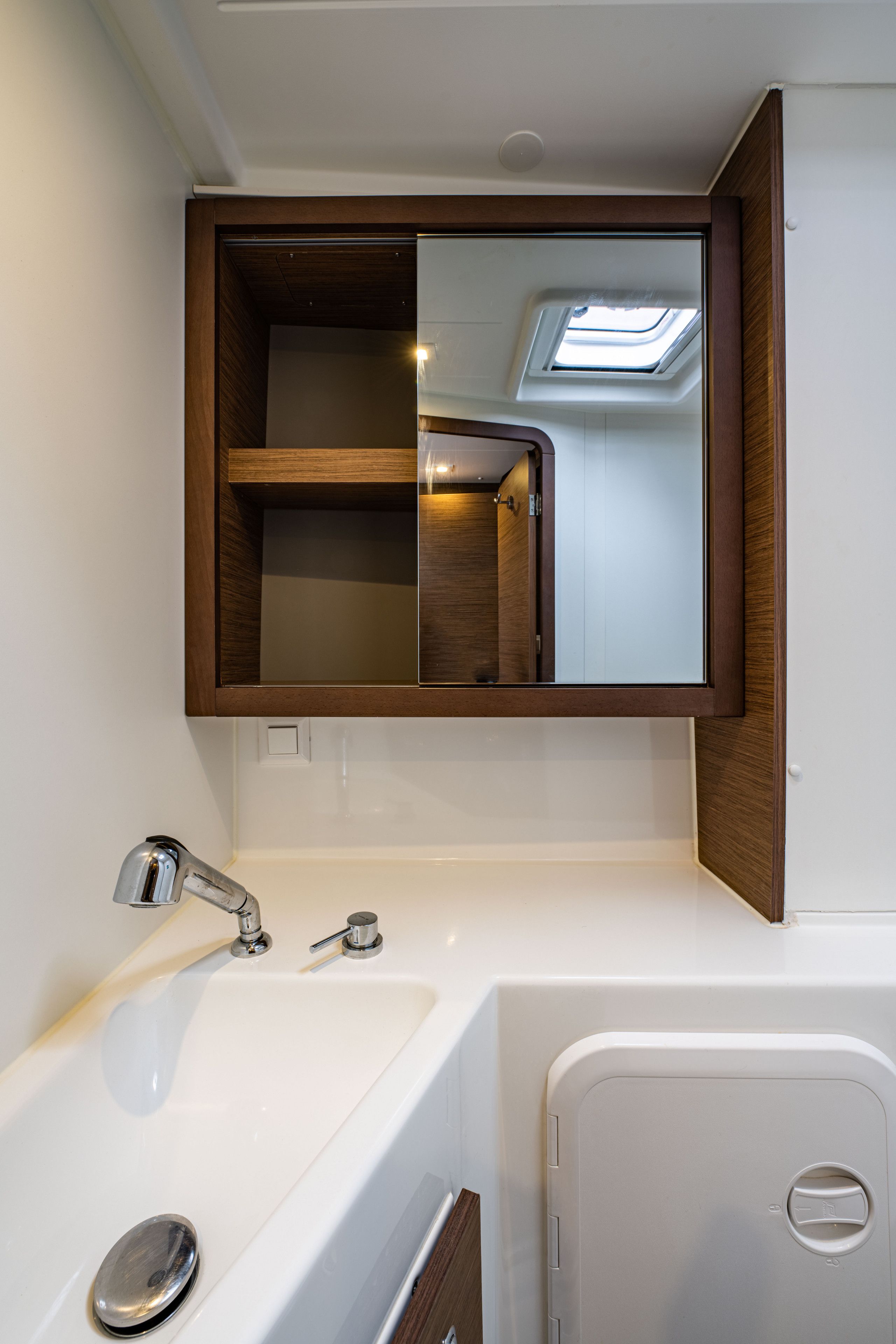 A bathroom with a white sink, a mirror, and a skylight.