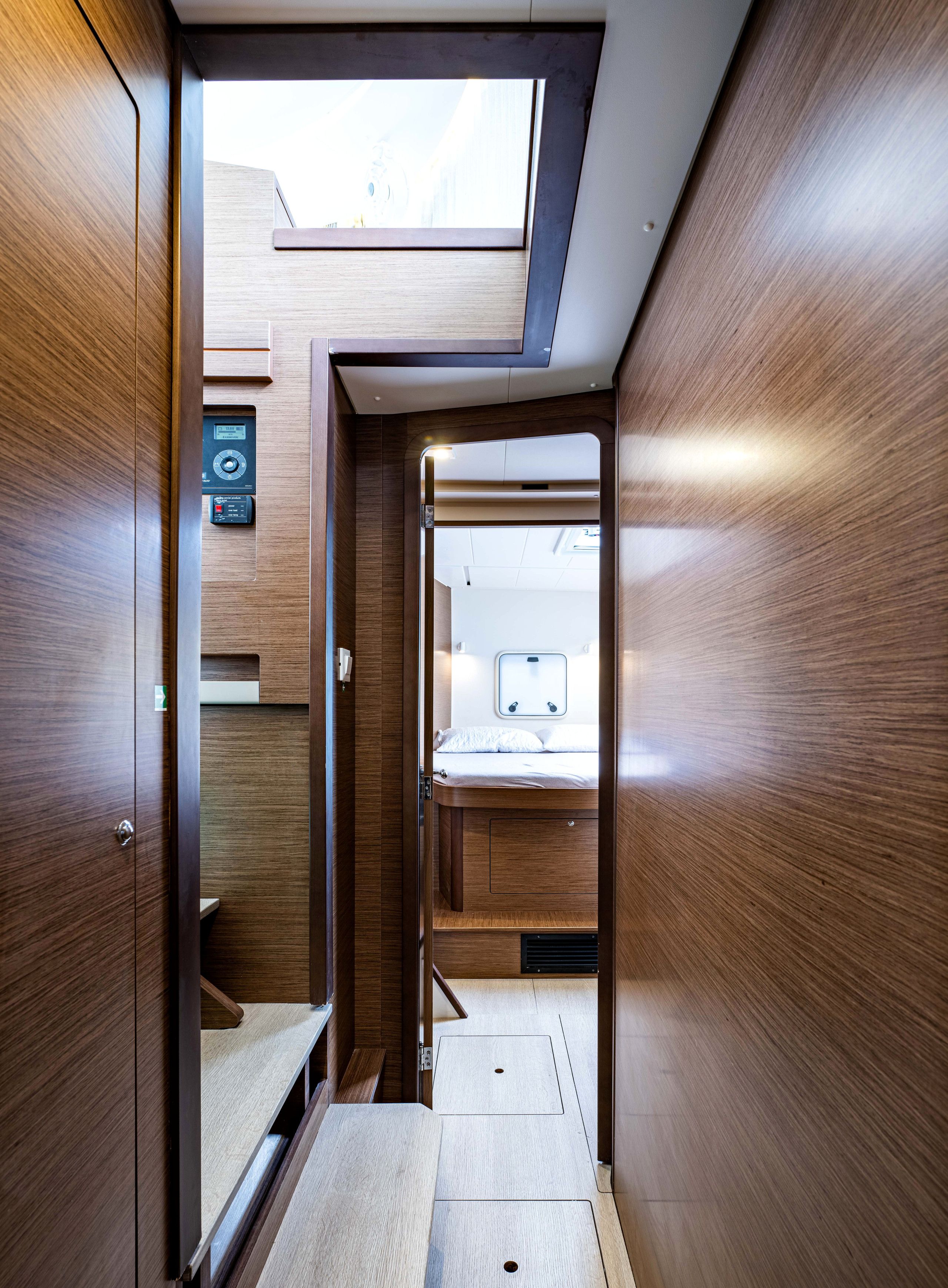 A narrow hallway with wooden walls and a skylight, leading to a bed area with a headboard and a control panel.