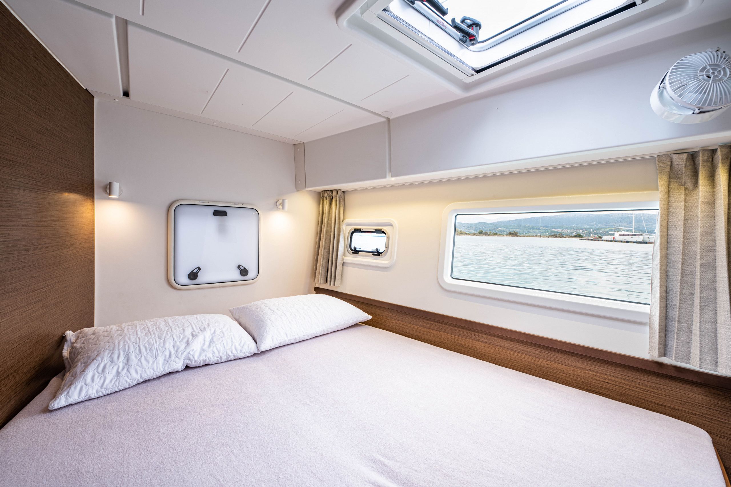 A bedroom with a bed, a window with curtains, a skylight, and a view of the water.