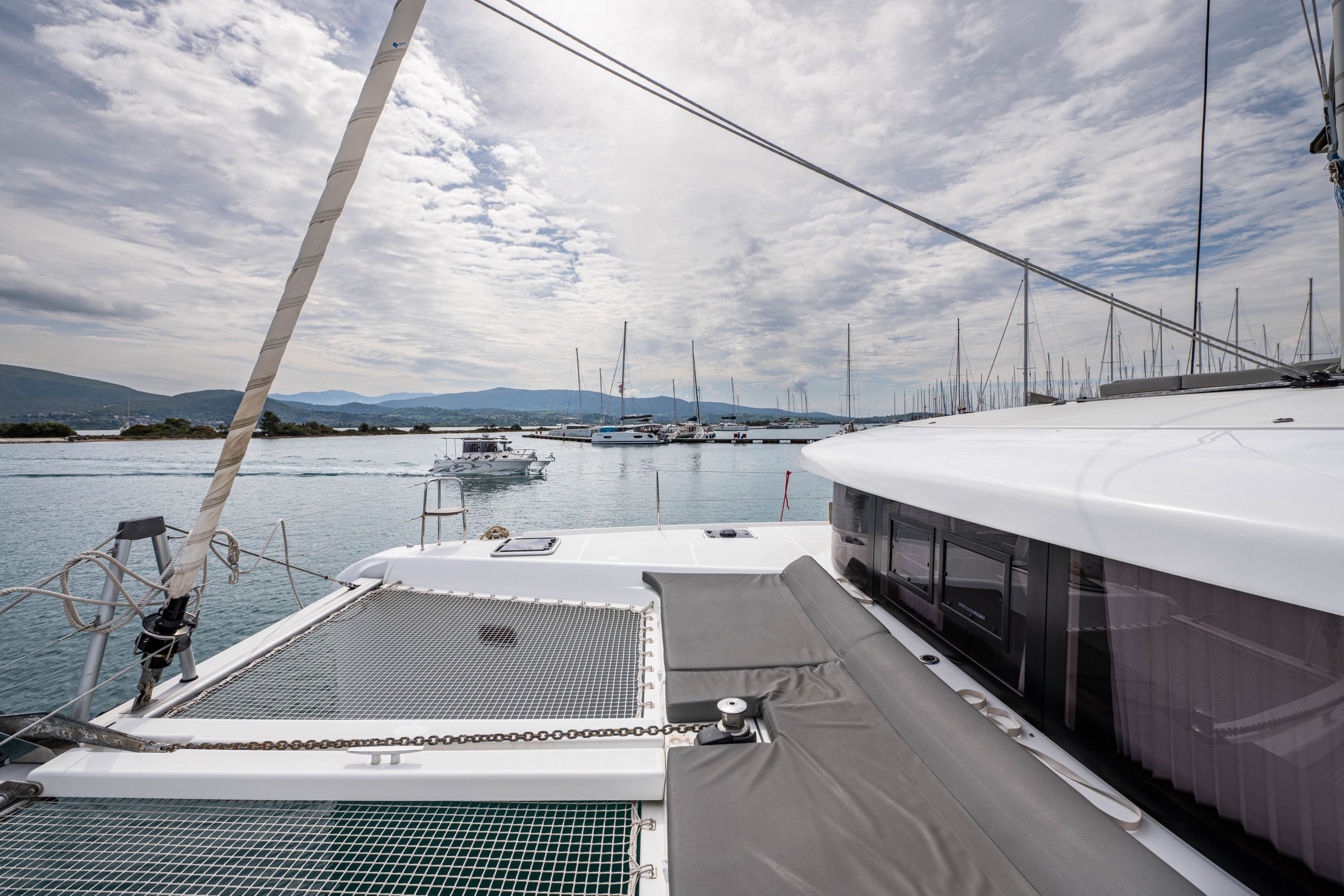 A yacht deck with a covered seating area, a mast, and a view of the marina with other boats.