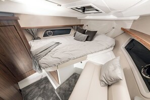 Ein gemütliches, helles Zimmer mit Bett, einer kleinen Sitzecke und einem Fenster mit Vorhängen.