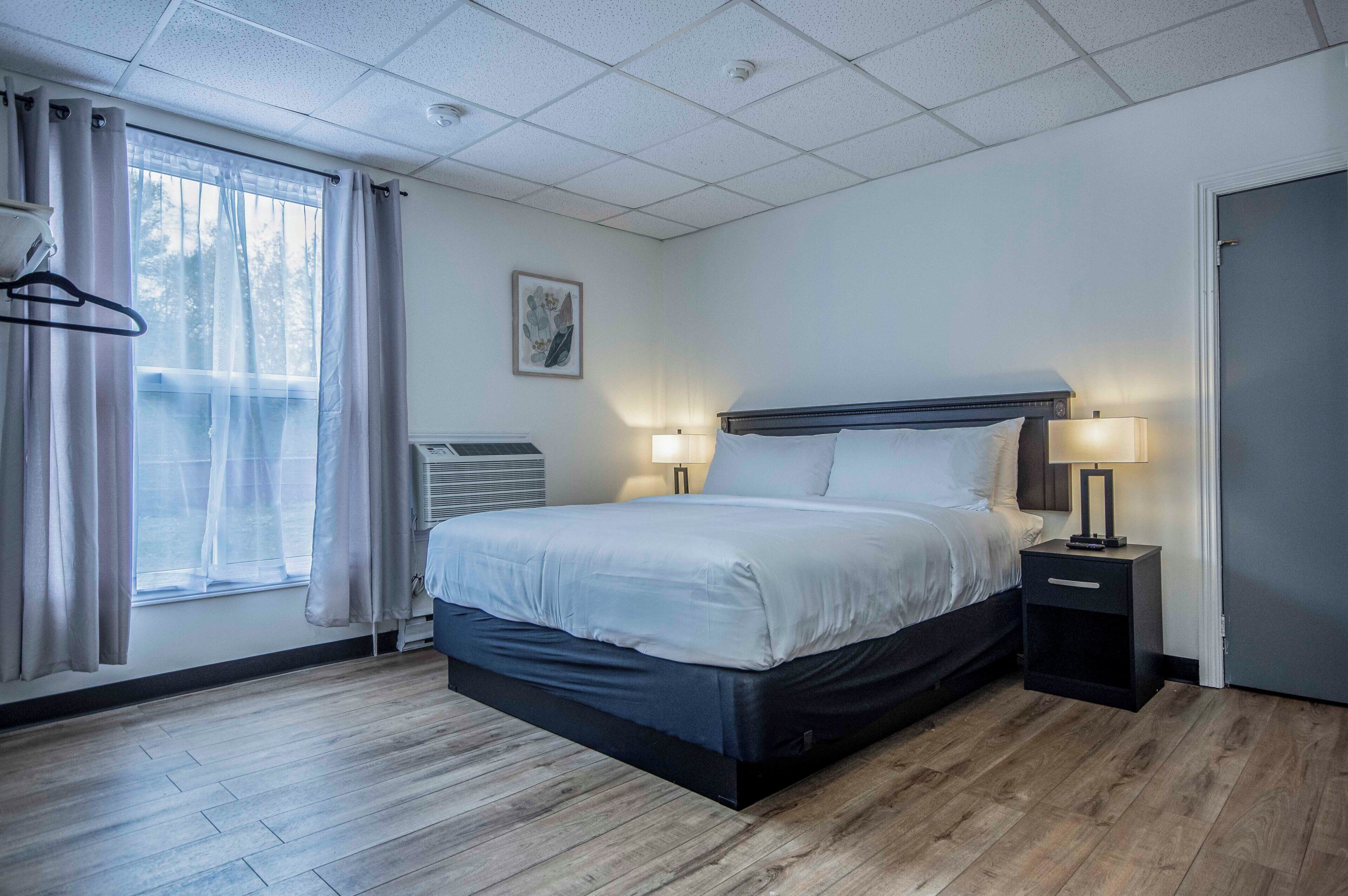 Ein Hotelzimmer mit Bett, Nachttischen, einem Fenster mit Vorhängen, einem Wandbild und einer Tür.