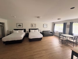 Habitación de hotel con dos camas, un sofá, una mesa de comedor y un ventanal con cortinas.