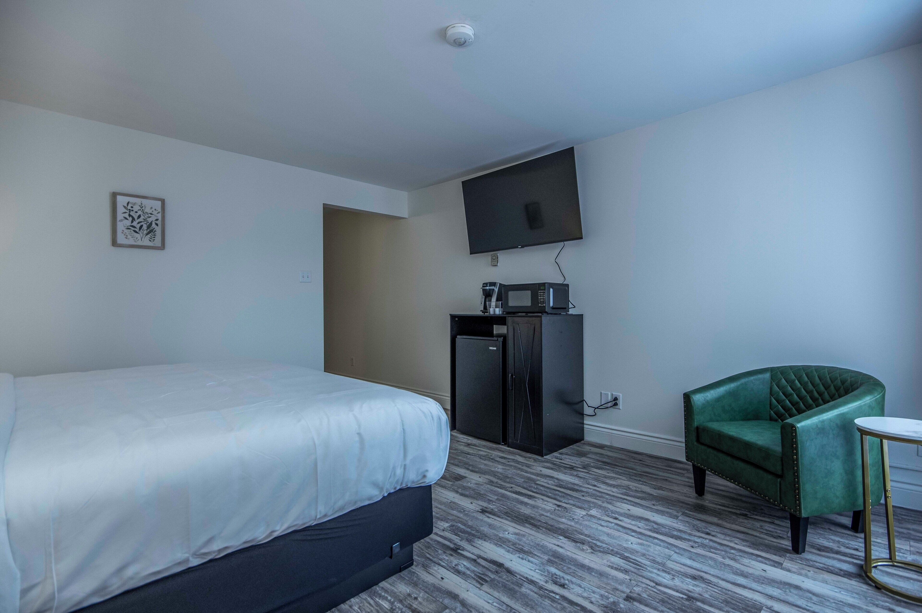 Una habitación de hotel con cama, escritorio, silla, televisor y un refrigerador pequeño.
