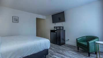 Una habitación de hotel con cama, escritorio, silla, televisor y un refrigerador pequeño.