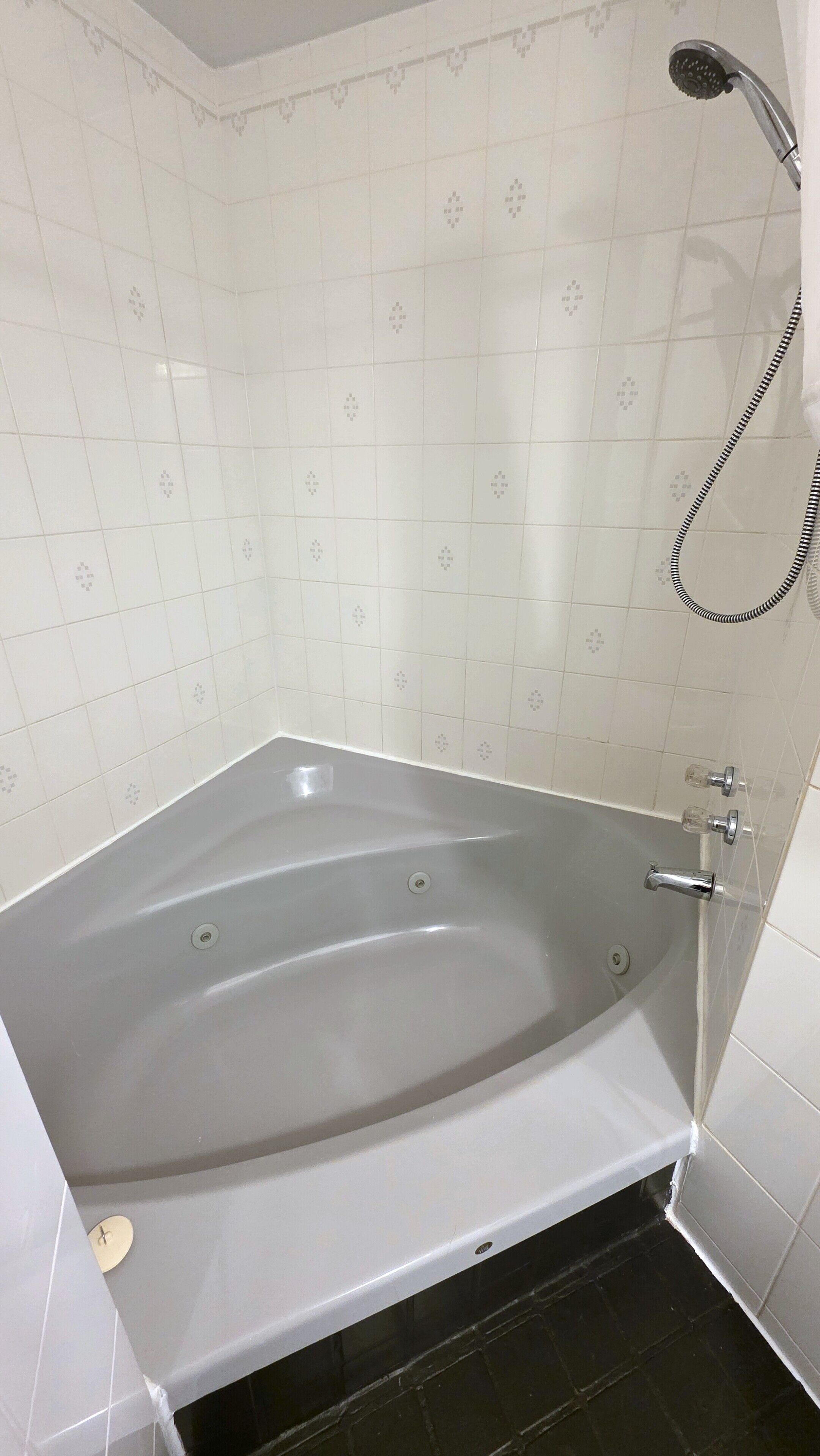 A bathtub with a shower head and controls, tiled walls, and a drain.