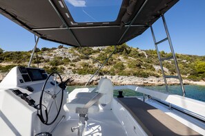 A boat's interior with a steering wheel, control panel, and a view of rocky coastline and water. - Sun-Kissed Sailing Adventure in Sibenik, Croatia (Primošten)