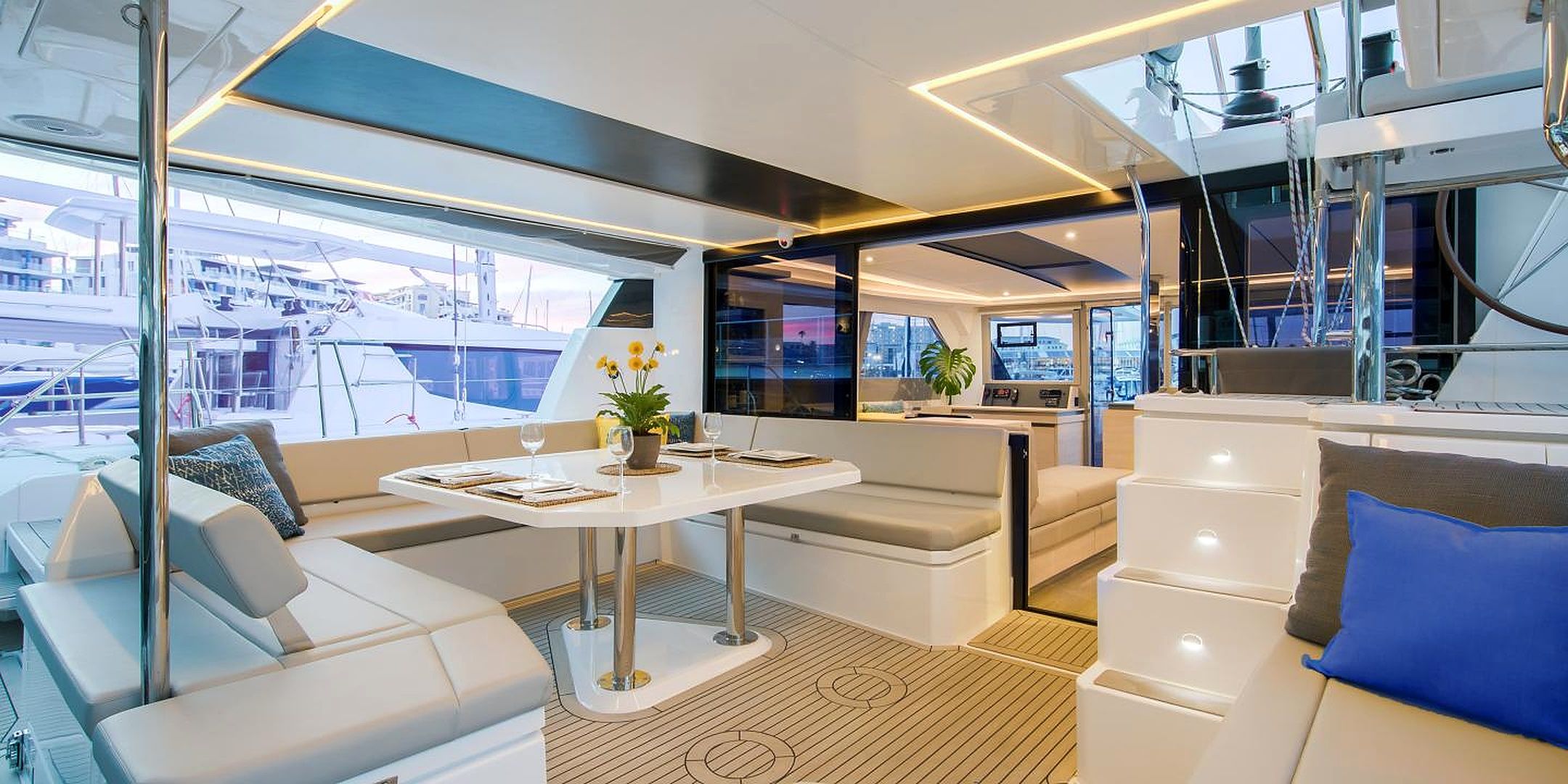 A modern yacht interior with a dining area, seating, and a view of the marina.