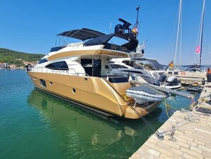 Eine große Yacht liegt in einer Marina mit blauem Himmel und ruhiger Wasserfläche.